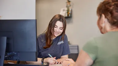 woman at desk writing in front of client