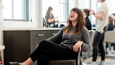 woman sitting in chair laughing in salon