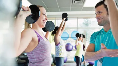 A male trainer teaching a woman lifting weights