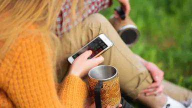 woman in yellow sweater holding smartphone outside
