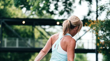 Woman stretching in running clothes on a path in front of a bridge