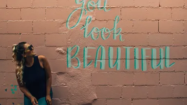 Woman leaning on a painted brick wall with a "You look beautiful" mural
